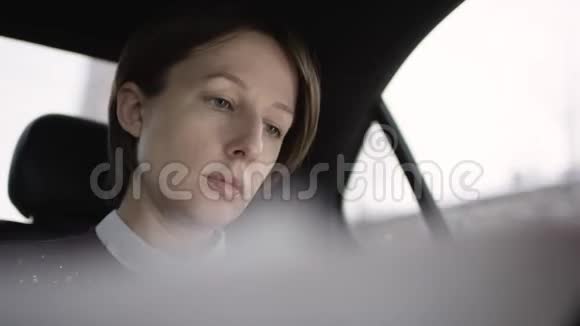 穿着白色上衣和栗色毛衣的棕色头发的漂亮女人坐在车里用电话谈论视频的预览图
