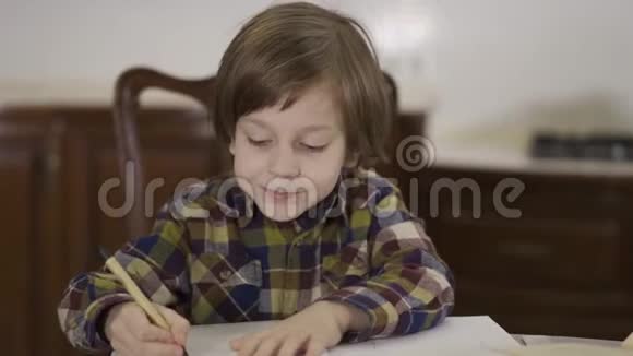 肖像可爱有趣的小男孩穿着格子衬衫坐在家里的桌子上做作业学生在画视频的预览图