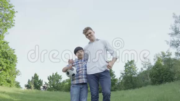 那个孩子抱着足球和爸爸在公园里看镜头拥抱家庭休闲户外活动孩子和视频的预览图