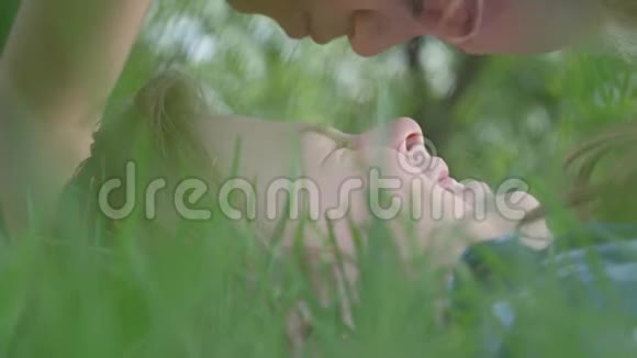 特写肖像可爱的小女孩亲吻额和鼻子的男孩躺在草地上一对快乐视频的预览图