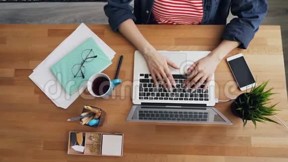 在木制办公桌上使用笔记本电脑在办公室打字的女性的最高视角视频的预览图