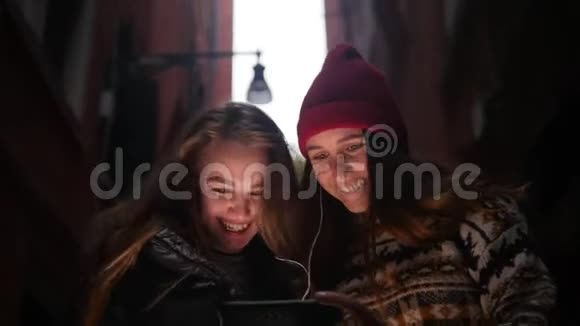 两个微笑的年轻女子走在街上戴着耳机看着手机屏幕视频的预览图