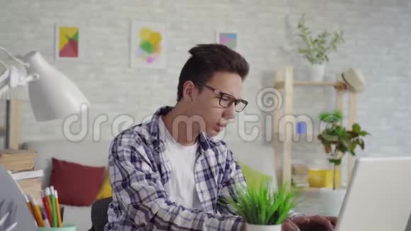 穿着衬衫脖子疼的年轻人坐在笔记本电脑前视频的预览图