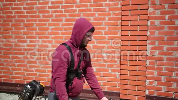 戴安全眼镜的人沿着高高的砖围栏割草机视频的预览图
