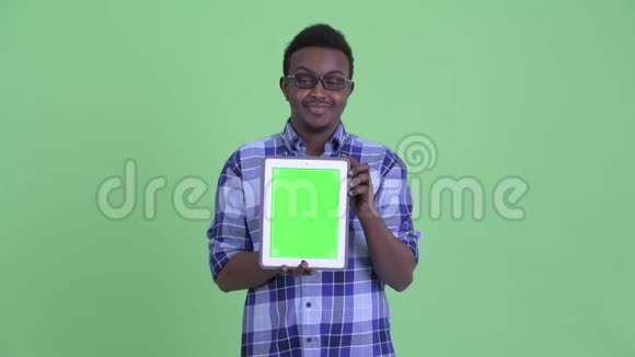 年轻快乐的非洲时髦男人一边思考一边展示数码平板电脑视频的预览图