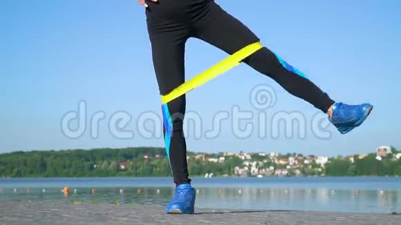 穿着运动装的女运动员使用弹性带双腿伸展全身靠近湖边年轻女孩在做视频的预览图