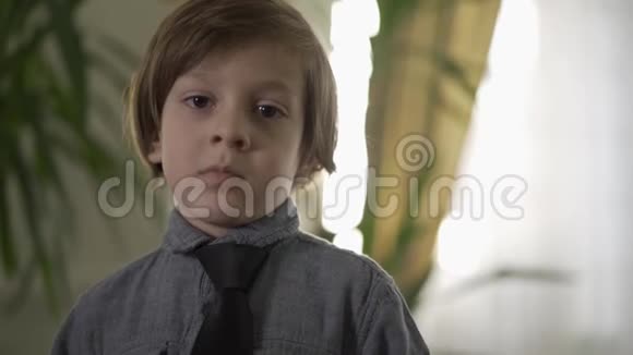 一幅可爱的严肃的小男孩的画像脖子上系着黑色领带两臂撑在窗前视频的预览图