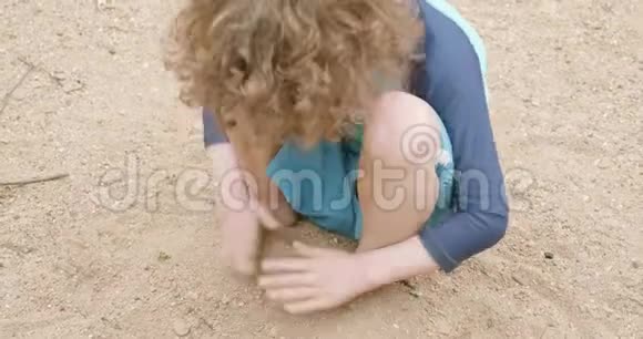 穿着蓝色泳装的小男孩在沙滩上用沙子盖住他的脚视频的预览图