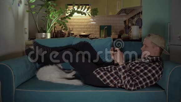 快乐的男人和猫躺在沙发上玩手机游戏4公里视频的预览图
