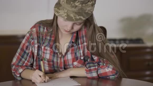 年轻女孩坐在家里的桌子上戴着士兵帽写着一封信视频的预览图