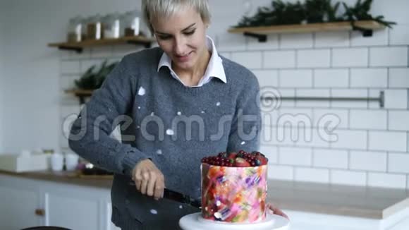 灰色头发的女人用刀从漂亮的蛋糕上切下一小块甜点是用浆果装饰的视频的预览图