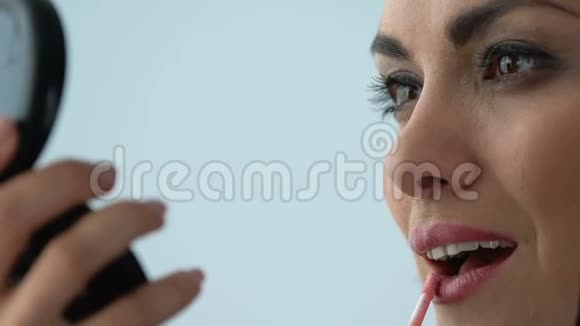 漂亮的女性涂上粉红色的唇膏看着手里的镜子防老妆视频的预览图