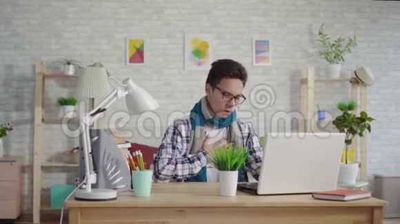 一个穿着衬衫喉咙痛坐在笔记本电脑前的冷酷的亚洲年轻人视频的预览图