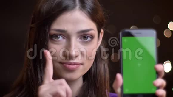 特写照片上年轻漂亮的白种人女孩拿着手机指着绿色屏幕竖起大拇指视频的预览图