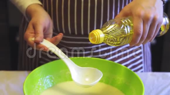 在家庭厨房的绿色碗里女性手的特写慢动作将葵花籽油添加到面糊中烹饪煎饼视频的预览图