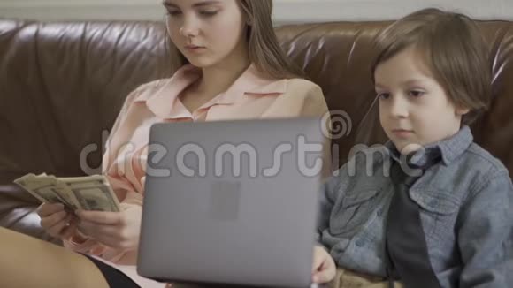 姐姐和弟弟坐在皮革沙发上的肖像那个拿着笔记本的男孩那个女孩视频的预览图