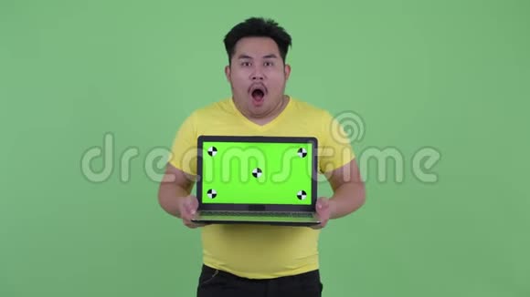 快乐的年轻超重的亚洲男人带着笔记本电脑看上去很惊讶视频的预览图