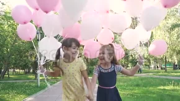 两个小女孩兴高采烈地跑过夏天公园手里拿着气球小妹妹们手牵手视频的预览图