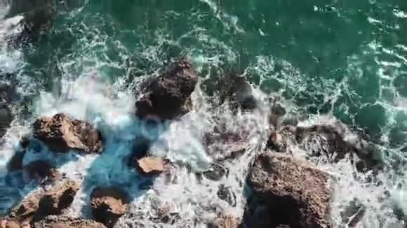 高空俯视蓝色海浪撞击岩石海岸创造白色泡沫和飞溅海浪随着岩石崩塌视频的预览图