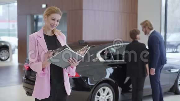 穿着粉红色夹克的讨人喜欢的女人的肖像在夫妇选择车辆之前有一本关于汽车的大书男人打开了视频的预览图