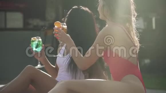 在阳光明媚的一天朋友们在户外放松和喝鸡尾酒穿泳衣的漂亮年轻女孩两个女朋友视频的预览图