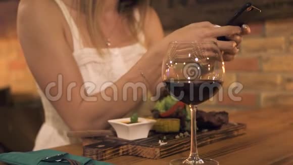 年轻女子在烧烤餐厅吃饭时使用智能手机晚上妇女通过手机浏览网络视频的预览图