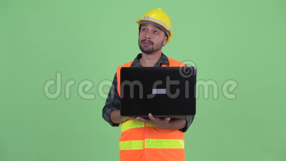 快乐的年轻人留着胡子的波斯建筑工人一边用手提电脑一边思考视频的预览图