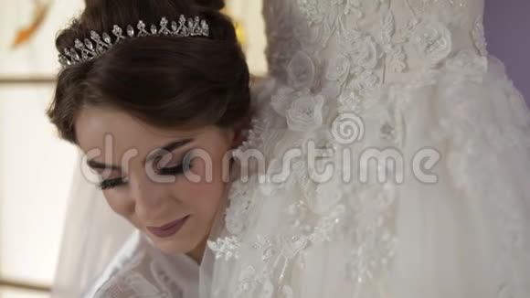 美丽可爱的新娘穿着睡衣站在婚纱附近看着相机微笑特写镜头视频的预览图
