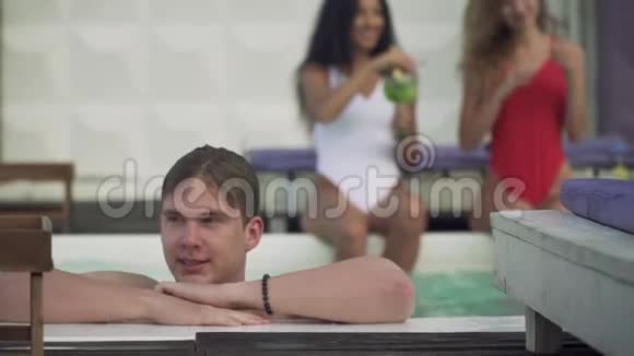 潮湿的年轻人在两个漂亮女孩的背景下在户外游泳池放松一群年轻人视频的预览图