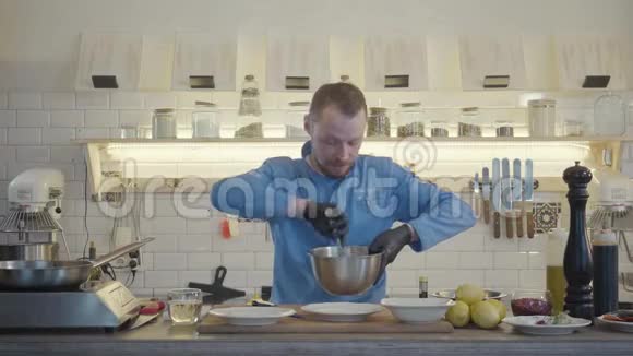 专业厨师戴着黑色橡胶手套用勺子把沙拉和调味料混合在铝碗里视频的预览图