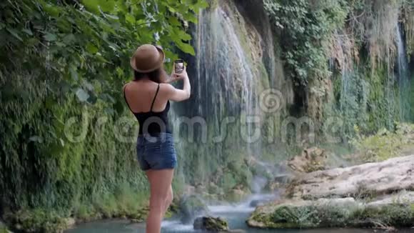 女帽后景拍照智能手机共享瀑布自然照片视频的预览图