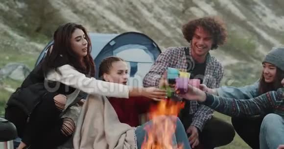 可爱的朋友在大自然C坐在篝火旁喝着五颜六色的杯子里的饮料他们有一个视频的预览图