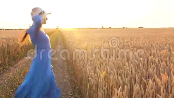 日落时分一个穿着蓝色连衣裙和帽子的漂亮女人正在麦田中央旋转自由概念小麦视频的预览图