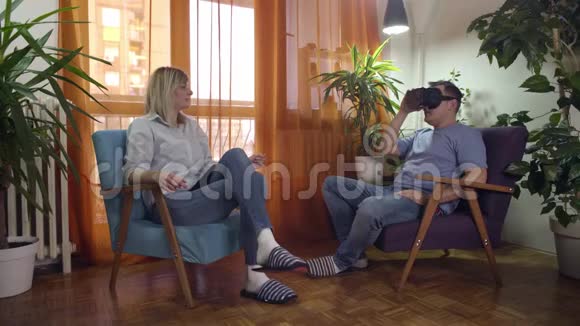男人和女人坐在现代的扶手椅上在家里分享虚拟现实的护目镜视频的预览图