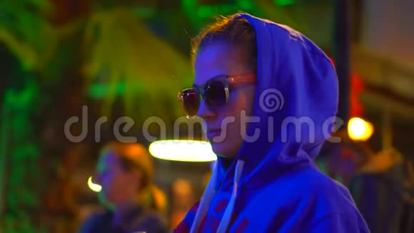 一个戴着头巾和眼镜的女孩站在城市灯光下的霓虹灯中用老式相机拍照视频的预览图