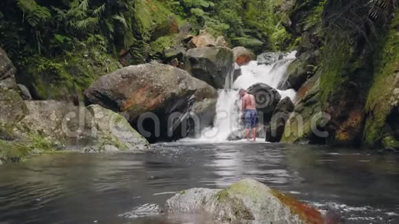 在热带雨林的热带瀑布景观上旅行的人游客站在背景流动的山河上视频的预览图
