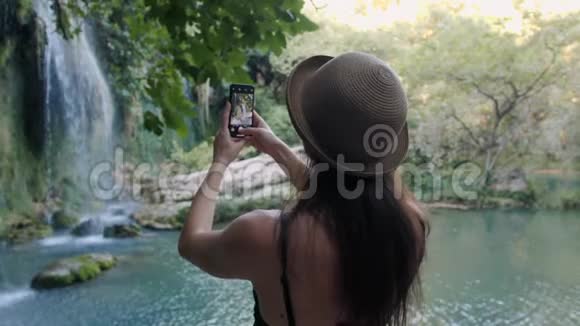 女帽后景拍照智能手机共享瀑布自然照片视频的预览图