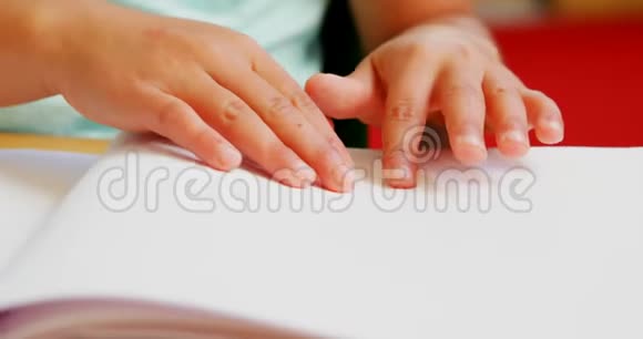 盲人高加索小学生在学校4k教室的课桌上读一本盲文书视频的预览图