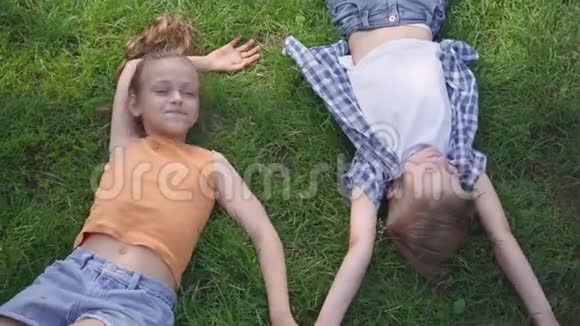 两个可爱的可爱孩子躺在公园的草地上互相微笑的肖像有趣的女孩牵着视频的预览图