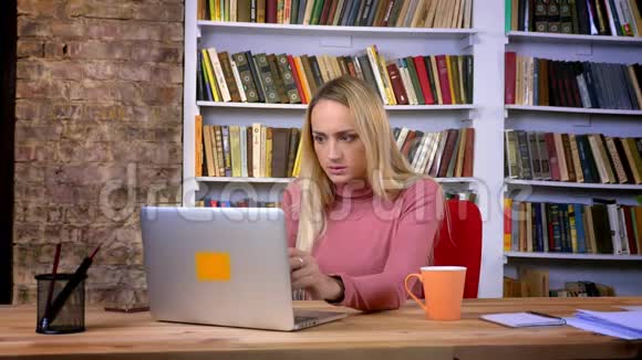 惊慌失措的白种人女孩的肖像穿着笔记本电脑工作在书架背景上面临麻烦视频的预览图
