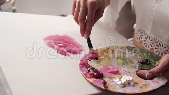 特写女孩用画笔和手指在画布上画粉红色的花视频的预览图