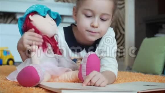 可爱的留着卷发的小女孩穿着孩子们睡衣躺在地板上的针织地毯上她自己在读一本视频的预览图