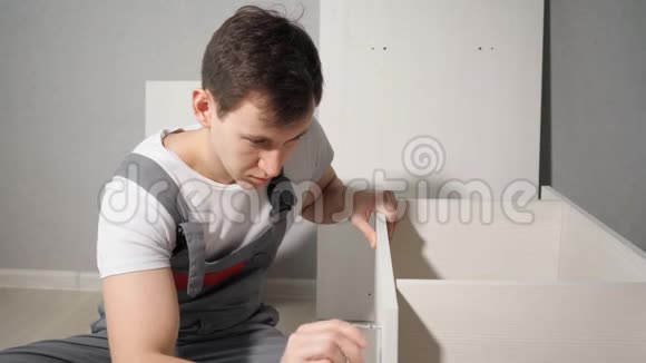 一个穿着工服的人在新家里坐在地板上组装家具视频的预览图