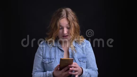一张成年白人金发女性的特写照片她在社交媒体上发帖时用手机看镜头视频的预览图