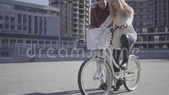 穿着棕色外套的帅哥在城里教女友骑自行车两人都笑了闲暇视频的预览图