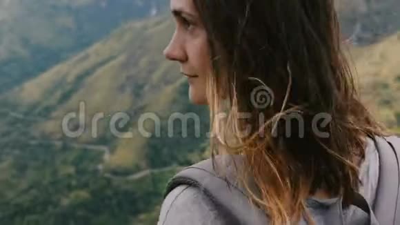 特写镜头在史诗般的山景中环绕着年轻放松的女人背包享受着风吹在头发上的风视频的预览图