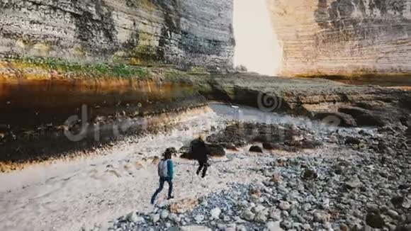 在诺曼底巨大的悬崖下探索令人惊叹的岩石卵石海滩的快乐游客夫妇的无人机追踪镜头视频的预览图