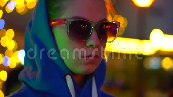 一个戴着头巾和眼镜的女孩站在城市灯光下的霓虹灯中用老式相机拍照视频的预览图