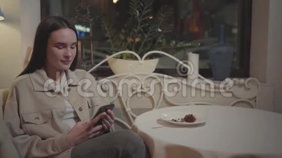 坐在饭馆桌子旁用手机发短信的美女肖像这块美味的蛋糕在视频的预览图