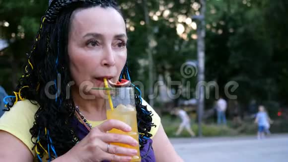 高级奢侈的女人喝着一杯激情水果鸡尾酒坐在公园里的一家街头咖啡馆里在树上视频的预览图
